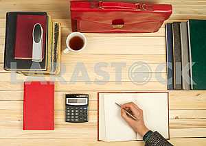 На деревянном столе книги, документы, калькулятор, красный портфель.