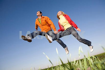Счастливая пара улыбаясь прыжков в небе над зеленый луг