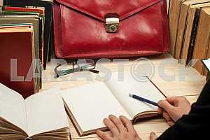 На деревянном столе книги, документы, калькулятор, красный портфель.