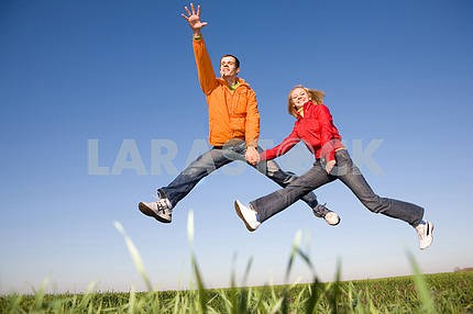 Счастливая молодая пара прыгает в небо над зеленый луг