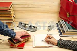 На деревянном столе книги, документы, калькулятор, красный портфель.