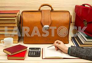 На деревянном столе книги, документы, калькулятор, красный портфель.