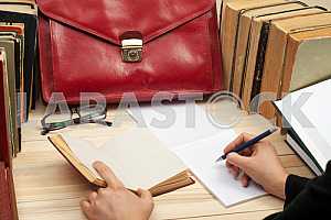 На деревянном столе книги, документы, калькулятор, красный портфель.