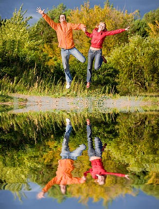 Счастливый молодая пара - прыжки в небо над оранжево- зеленый Tre