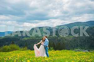 Свадьба в горах, пара в любви, фон горы, стоя в окружении одуванчики, среди газона с зеленой травой, деревенском стиле, девушка в длинном платье из тюля, романтический пейзаж
