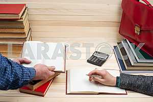 На деревянном столе книги, документы, калькулятор, красный портфель.