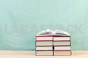 Открытая книга, стопка книг в твердом переплете на деревянном столе. Обратно в школу. Копирование пространства