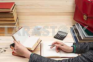 На деревянном столе книги, документы, калькулятор, красный портфель.