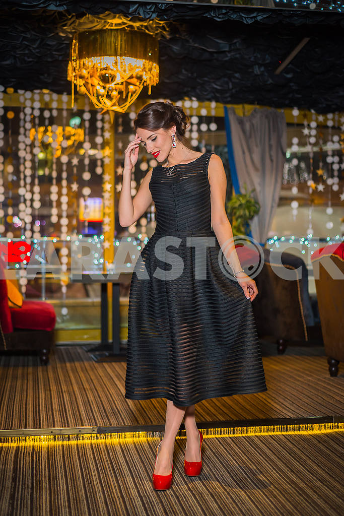 Beautiful brunette woman walking in the restaurant, in black dress and red shoes. Smiling with her red lips, shy like a little girl — Image 37632