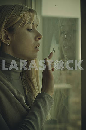 Young girl sitting by the window draws heart