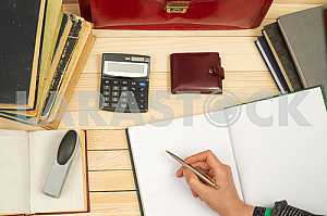 On a wooden table books, documents, calculator, red briefcase.