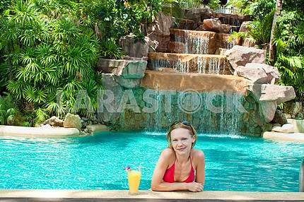 Happy young woman with an exotic cocktail in the pool