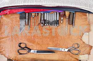 Leather craft tools on a leather background. Craftsman work desk . Piece of hide and working handmade tools on a work table. Top view. Copy space
