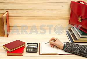 On a wooden table books, documents, calculator, red briefcase.