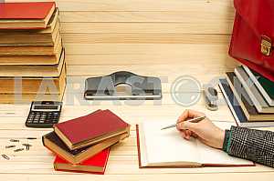 On a wooden table books, documents, calculator, red briefcase.