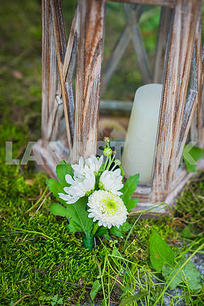 The wedding boutonniere for the groom made of white and green chrysanthemum  Vintage wooden lantern and moss on the background and a candle