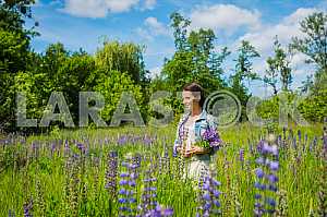 Young woman, happy, standing among the field of violet lupines, purple flowers. Blue sky on the background. Summer, sunny day!