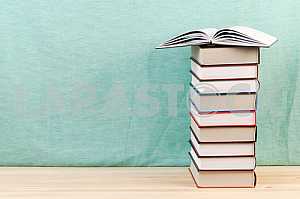 Открытая книга, стопка книг в твердом переплете на деревянном столе. Обратно в школу. Копирование пространства