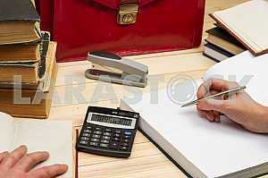 On a wooden table books, documents, calculator, red briefcase.