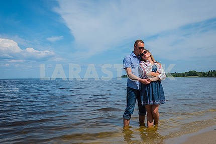 A loving couple standing in the river, embracing each other, blue sky on the background, sunny day, wide angle, long white clouds