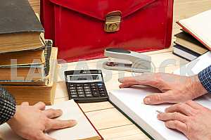 On a wooden table books, documents, calculator, red briefcase.