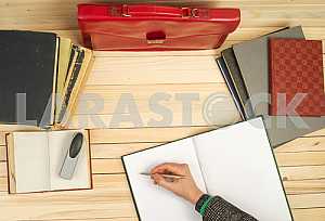 On a wooden table books, documents, calculator, red briefcase.