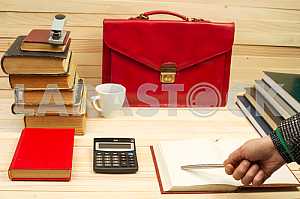On a wooden table books, documents, calculator, red briefcase.