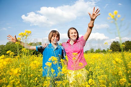 Girl and boy relaxing on meadow full of yellow flowers. Soft foc