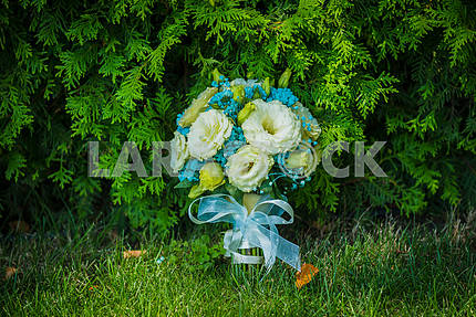 wedding bouquet standing near the thuja tree, with blue ribbon, green grass and some autumn leaves near