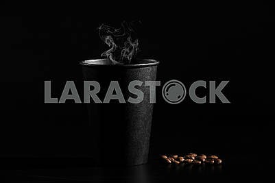 A black glass of hot coffee with scattered coffee beans on a black background. close-up