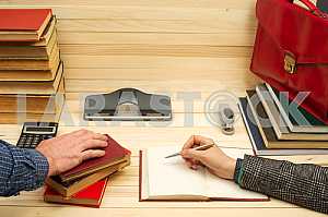 On a wooden table books, documents, calculator, red briefcase.