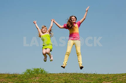 Two girls jumping on green meadow