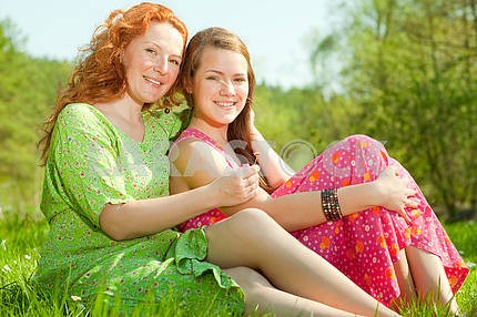 funny mother and daughter sitting on green grass