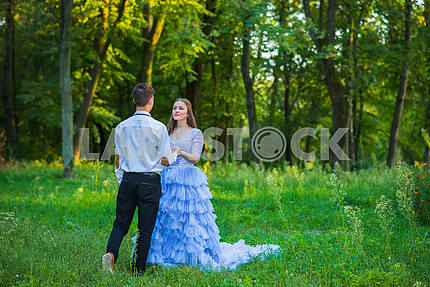 A love story couple, in love, together in the forrest park, girl in a beautiful violet dress, sunny evening, summer, thematic wedding shooting, frill dress