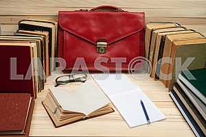 On a wooden table books, documents, calculator, red briefcase.