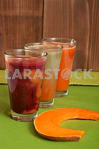 Various freshly squeezed vegetable juices with the hunk of pumpkin on green background.