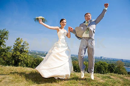 Groom and bride jumping against backdrop a sky and trees. In all