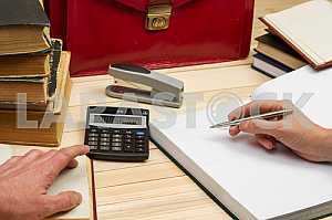 On a wooden table books, documents, calculator, red briefcase.
