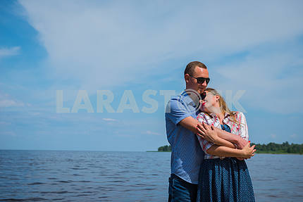 a loving couple standing in the river, embracing each other, blue sky on the background, sunny day, wide angle, long white clouds