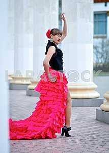 Woman Dancing carmen in saturated pink long curly skirt, with tied hair, and the flower in hair, in black blouse, among the column, showing her legs