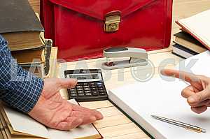 On a wooden table books, documents, calculator, red briefcase.