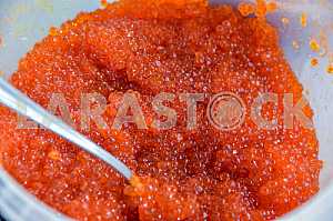 A bucket full of red caviar with spoon