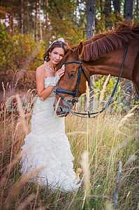 Bride brown-haired woman standing leaning to the horse, in wedding dress mermaid silhouette, among the spikelet, autumn, forest on the background
