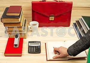 On a wooden table books, documents, calculator, red briefcase.