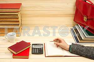 On a wooden table books, documents, calculator, red briefcase.