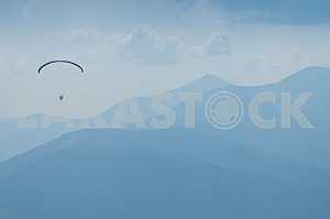 Paraglider flying over mountains on a summer day