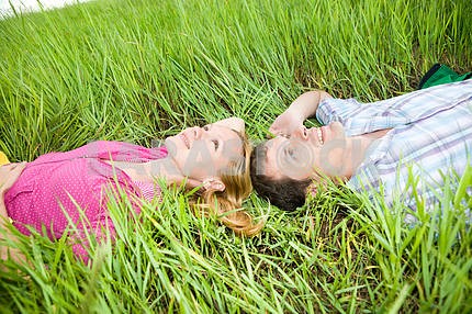 Young love couple lay on the green grass outdoors