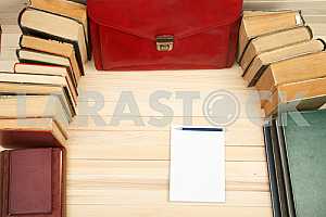 On a wooden table books, documents, calculator, red briefcase.