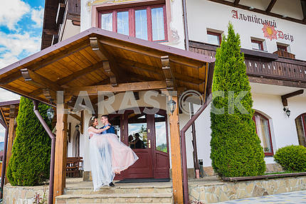 A wedding couple, groom holdin the bride on hands in the front of an entrance to an old hotel. sunny day, lovely couple. groom carrying bride