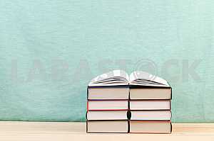 Открытая книга, стопка книг в твердом переплете на деревянном столе. Обратно в школу. Копирование пространства